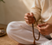 Hands holding a Rudraksha mala during seated mantra meditation